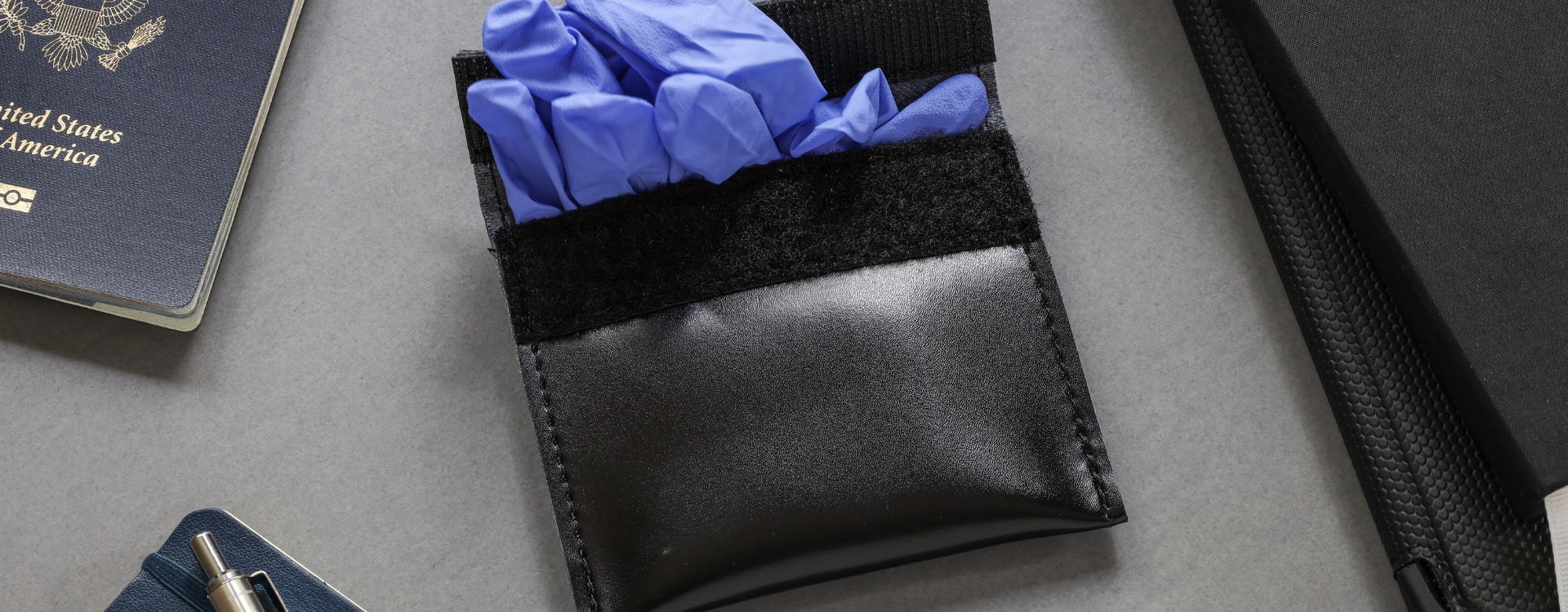 Black pouch with blue latex gloves on a gray surface next to a passport