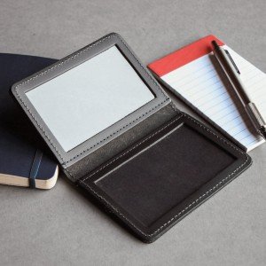 Black leather cardholder with a card and pen on a gray surface