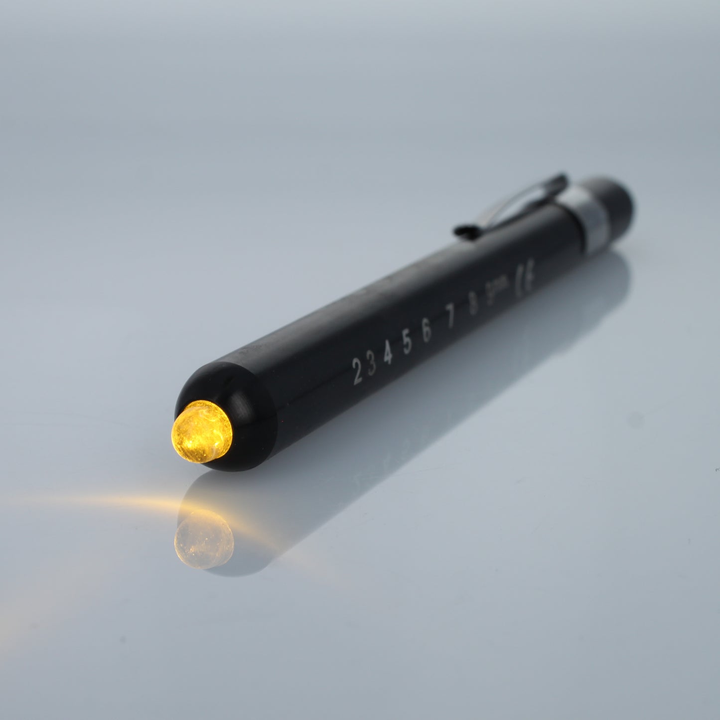 Black EMT diagnostic pen light illuminated with warm yellow LED.