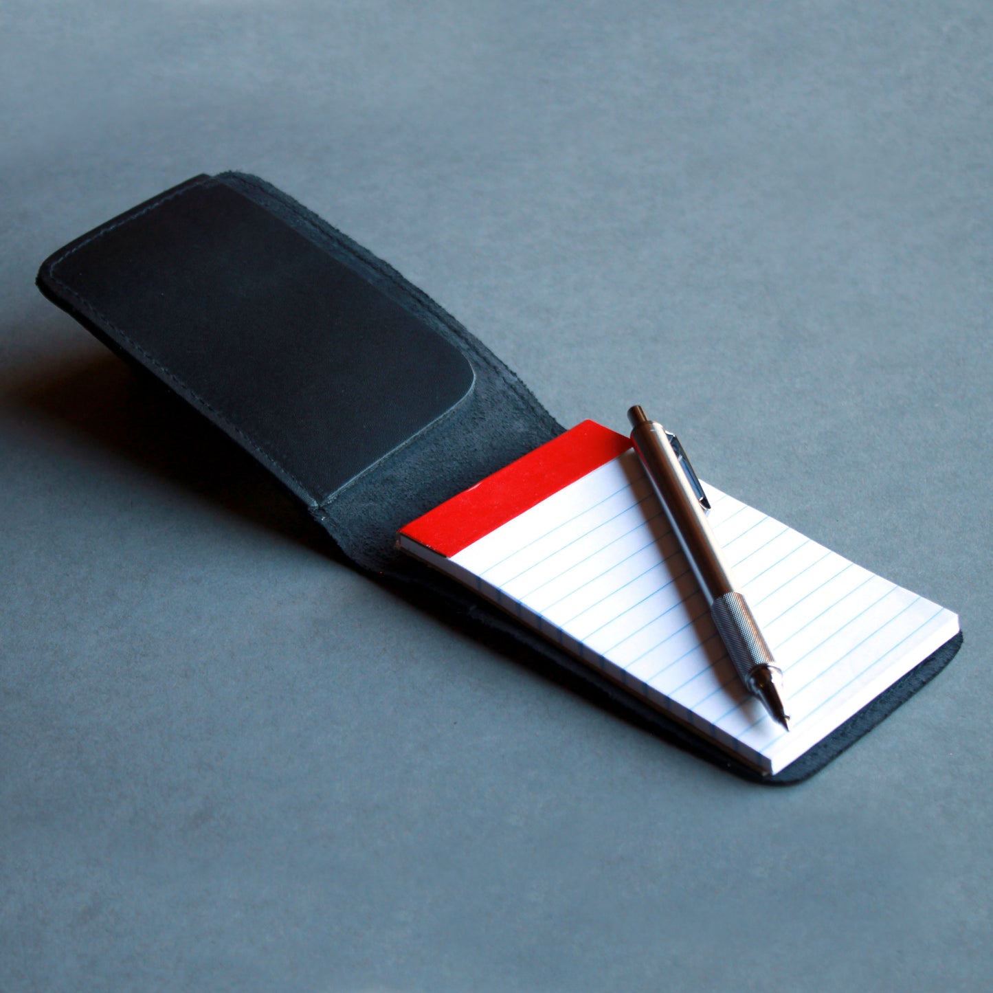 Open black leather notepad holder with paper pad inside.