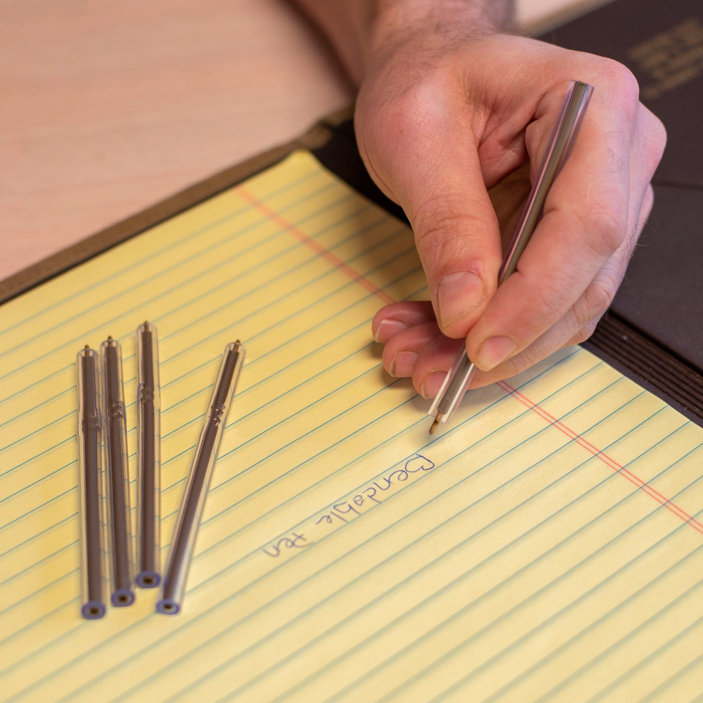 Hand placing multiple non-lethal flexible pens on yellow legal pad.
