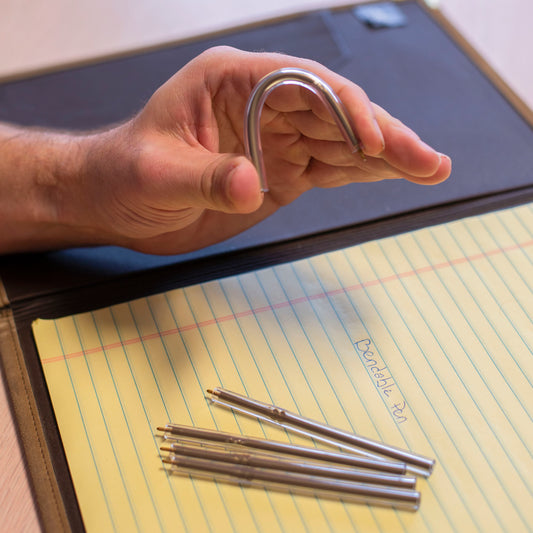 Two hands bending flexible pen above yellow notepad.