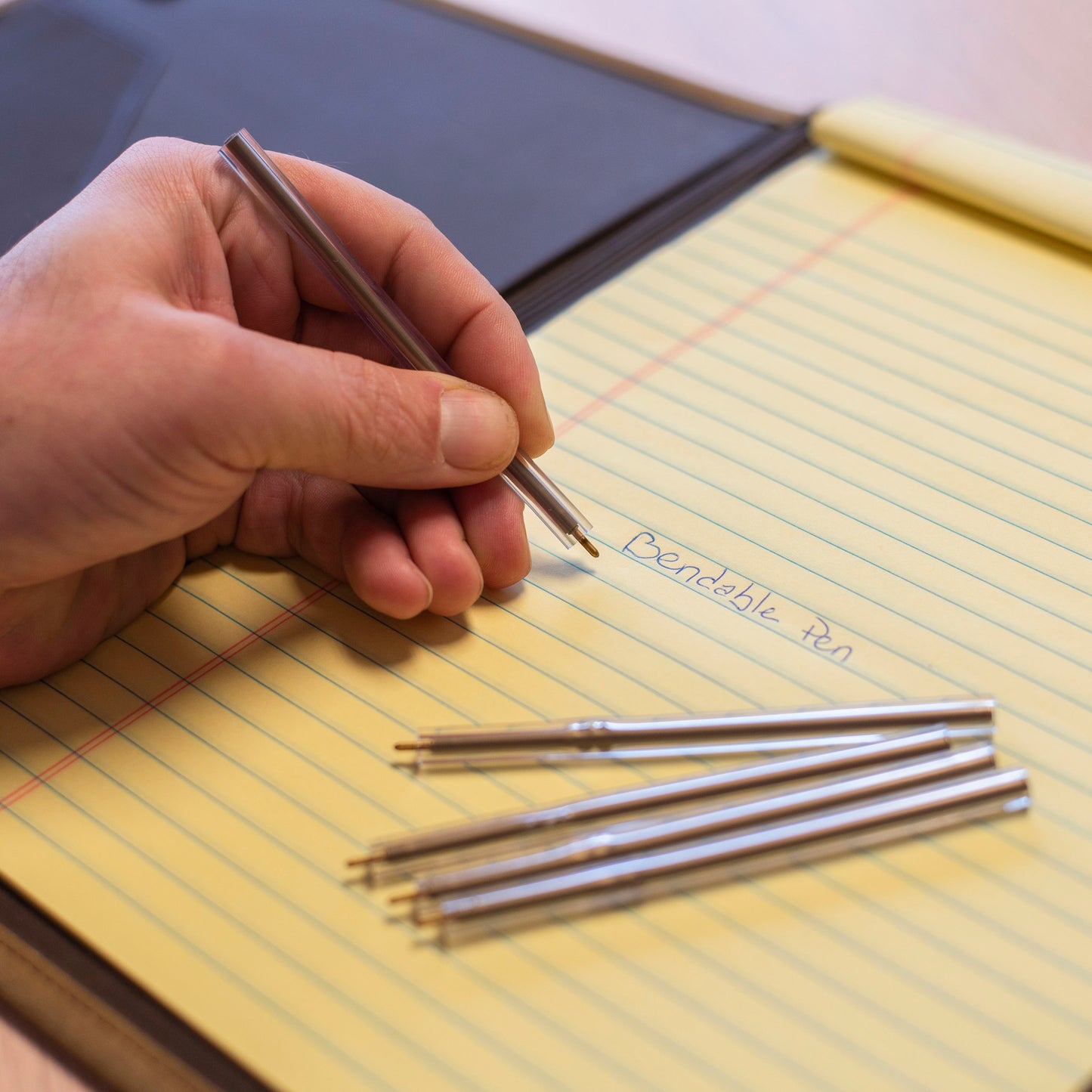 Hand arranging several flexible ballpoint pens on yellow legal pad.
