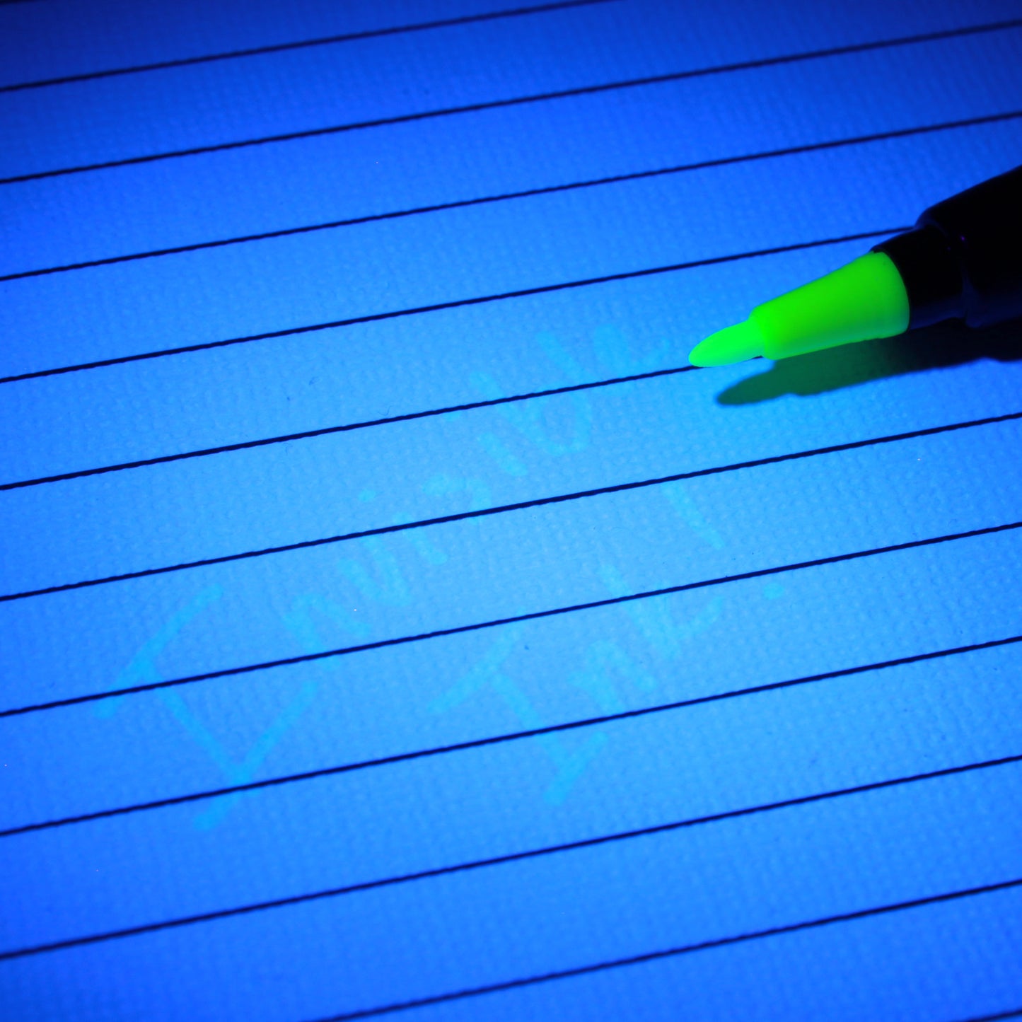 Green UV invisible ink pen writing on lined paper under blue UV light.
